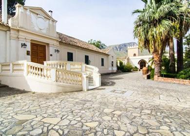 Antica villa con cortile in pietra e palme, immersa nella natura.